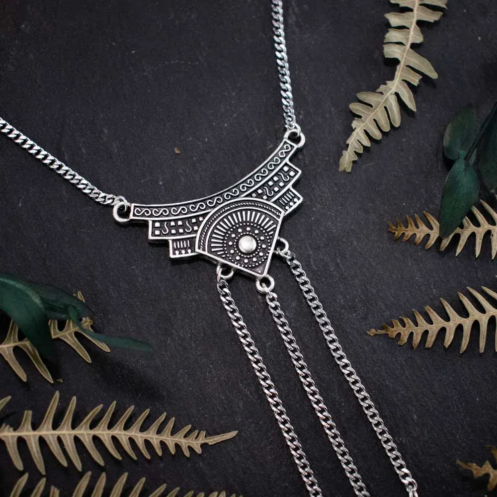 Close-up of nature goth jewelry showing the fluid movement of silver chains and sharp black quills against a rugged dark rock backdrop.