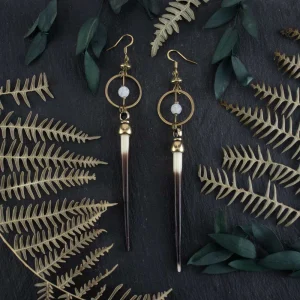 Modern cowgirl style earrings featuring natural porcupine quills, styled in a dark western aesthetic on a black textured background with forest elements.