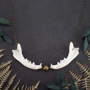 Flat lay of an ethnic bronze necklace featuring real feline jaw bones, carefully arranged on a black textured surface with dried forest ferns