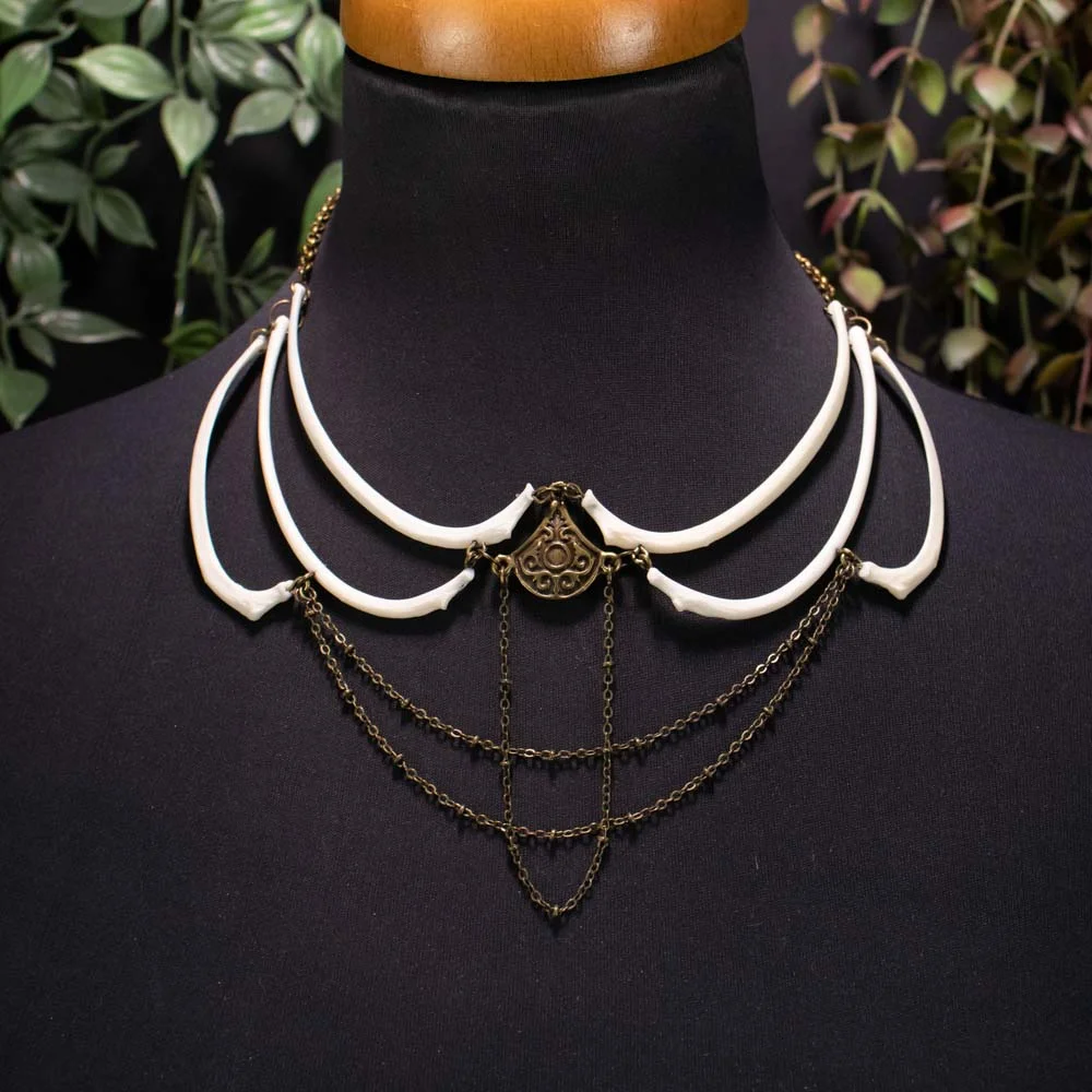 bronze ethnic necklace featuring real curved fox rib bones and hanging chains, presented on a black textured surface with dried ferns.