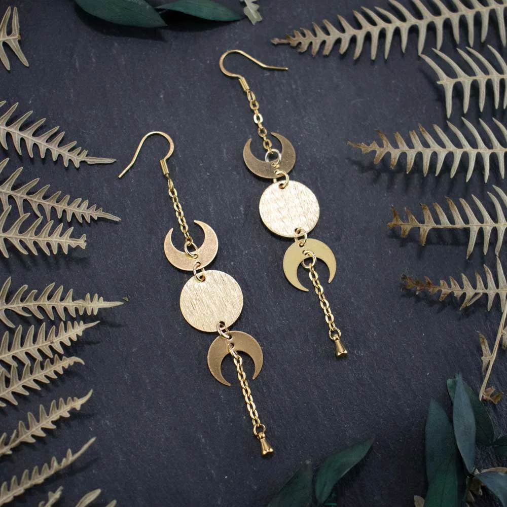 Detailed view of moon phase jewelry with a golden celestial drop and radiant lunar symbols, displayed on a dark, textured surface.