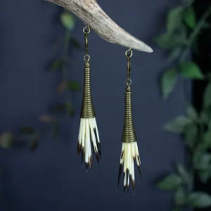 Handmade tribal chic earrings featuring rustic bronze cones and ethically sourced quills, showcased in a moody dark nature aesthetic with botanical elements.