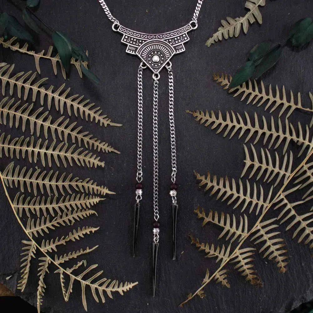 Detailed shot of a silver necklace with cascading chain drops and authentic black porcupine quills, styled on a dark textured slate background framed by shadowy dried ferns.