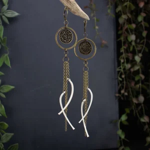 Handmade bronze jewelry with delicate chain drops and ethically sourced rib bones, showcased in a moody dark nature aesthetic with forest elements