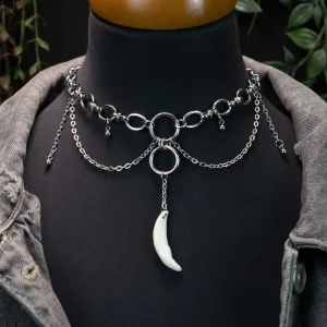 Gothic silver necklace with a real fox fang pendant and cascading chain drops, laid flat on dark charred wood with a moody atmosphere.