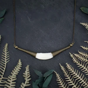 Detailed shot of the sharp, natural texture of a white fox fang pendant in a bronze cap.