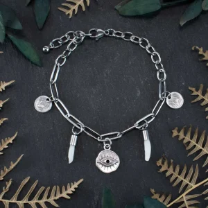 Handcrafted bone jewelry with protective evil eye charms styled on a black surface among dried foliage for a witchy look.