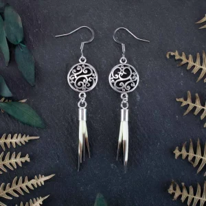 Macro view of multiple small porcupine quills and intricate silver metalwork against a backdrop of organic forest leaves.